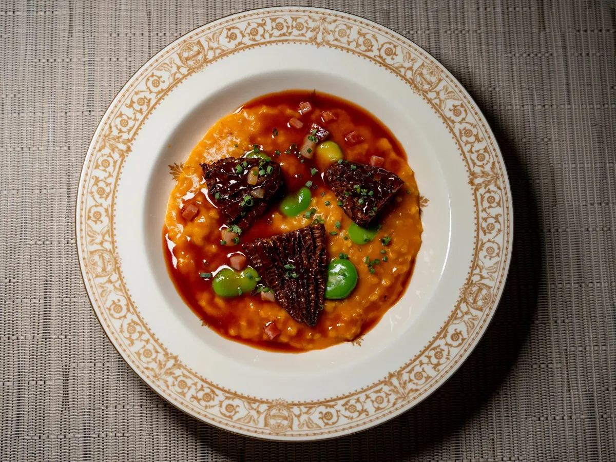 Seared beef in a red-orange sauce with sliced green chili on a gold-rimmed plate