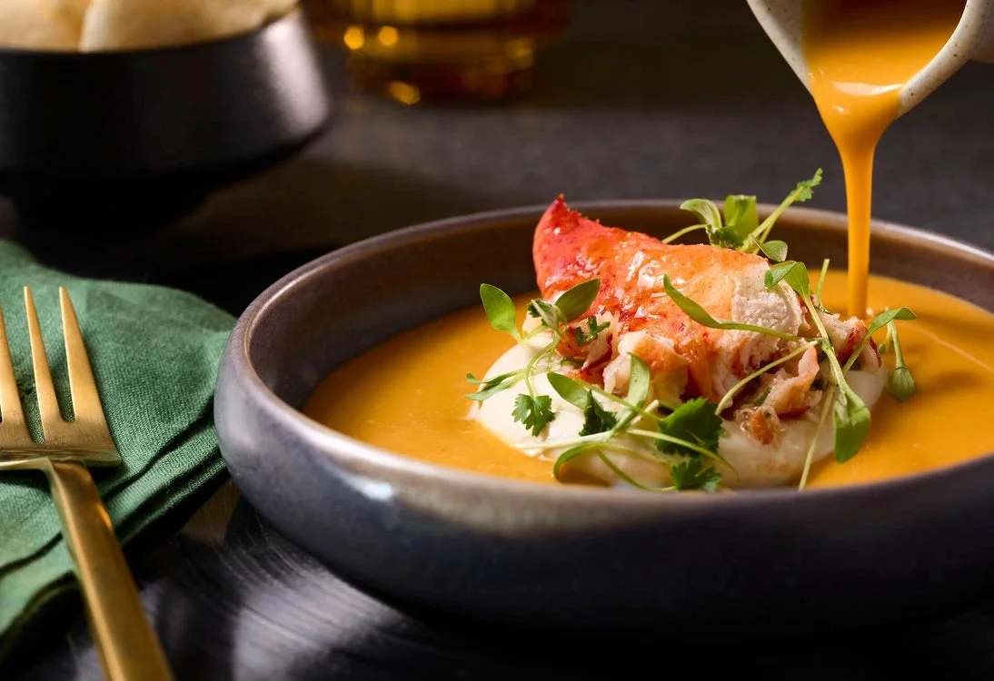 Sauce poured over a lobster salad in a dark bowl