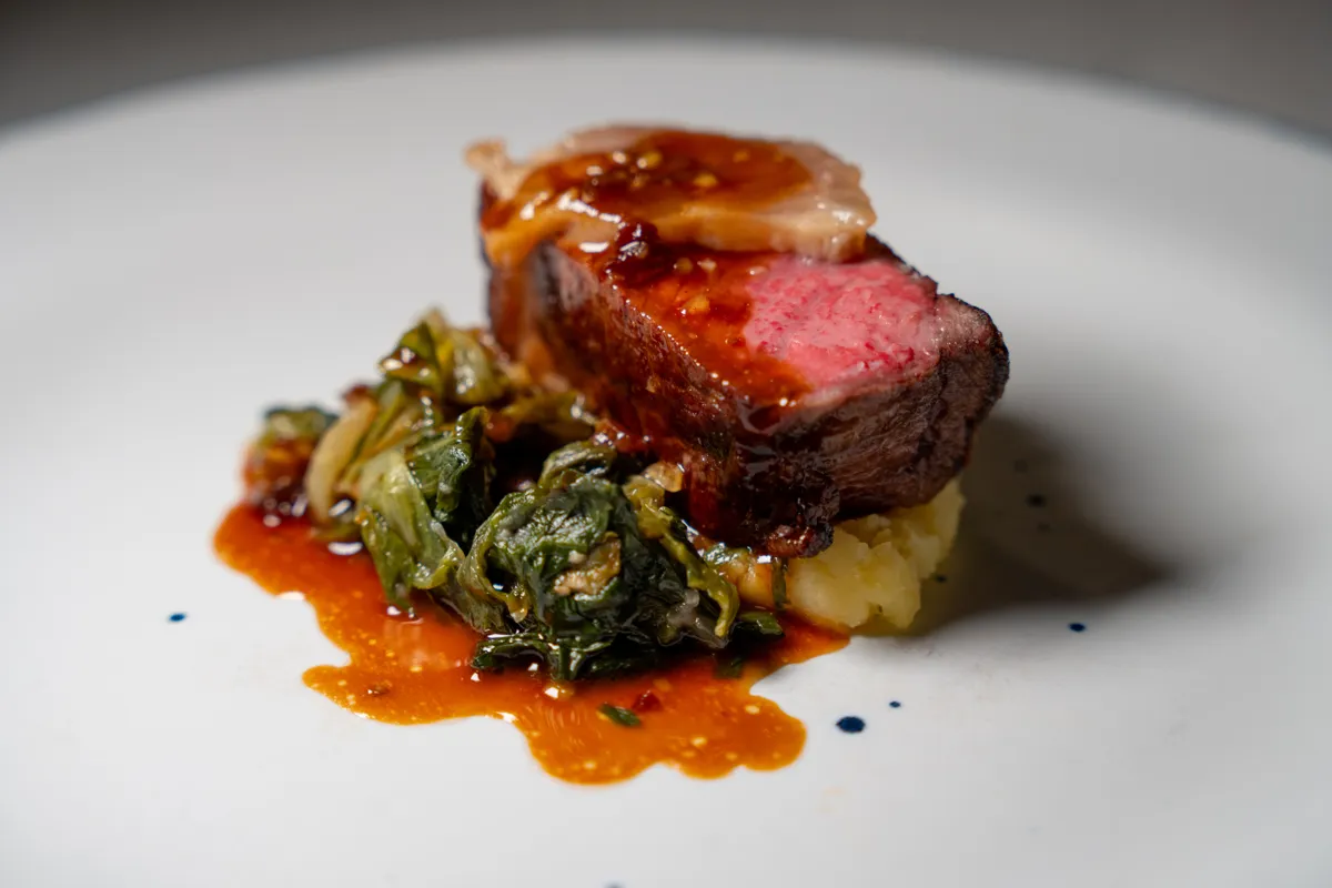 Roasted beef with braised greens, potato purée, and pan sauce