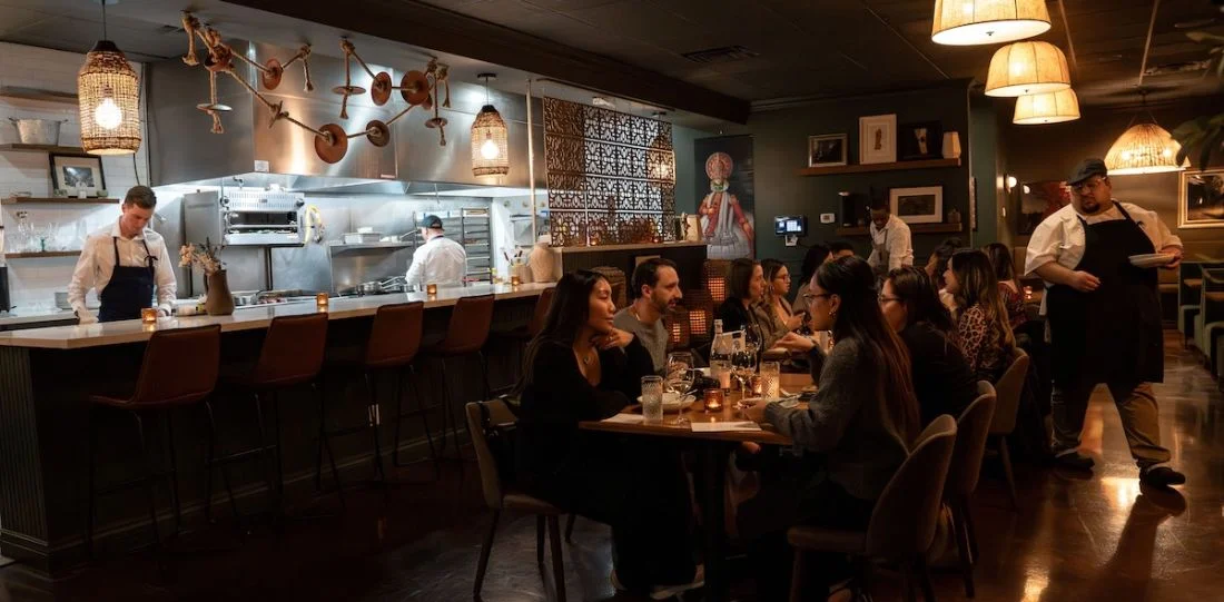 Diners in a restaurant dining room with an open kitchen behind them